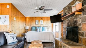 Une pièce confortable avec un lit, un canapé en cuir noir, une cheminée en pierre et un téléviseur fixé au mur.