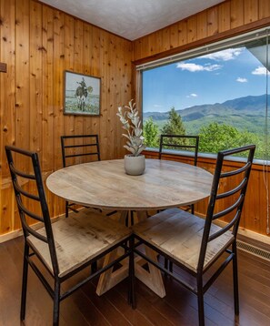Una habitación con paneles de madera, una mesa redonda con sillas, una planta en maceta y un cuadro en la pared.