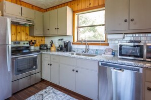 A kitchen with stainless steel appliances, white cabinets, and a window providing natural light.