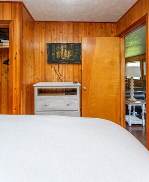 A bedroom with a wooden wall, a bed, a dresser, and a painting.