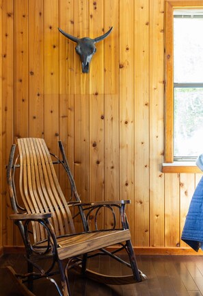A rustic wooden interior with a rocking chair and a bull skull mounted on the wall.