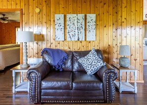 A room with a brown leather sofa, a patterned pillow, and a blue throw blanket. There are two side tables with lamps.