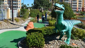 A dinosaur statue in a landscaped area with a pool table and a building in the background. - BEAUTIFUL RESORT STUDIO NEAR DISNEY (Kissimmee)