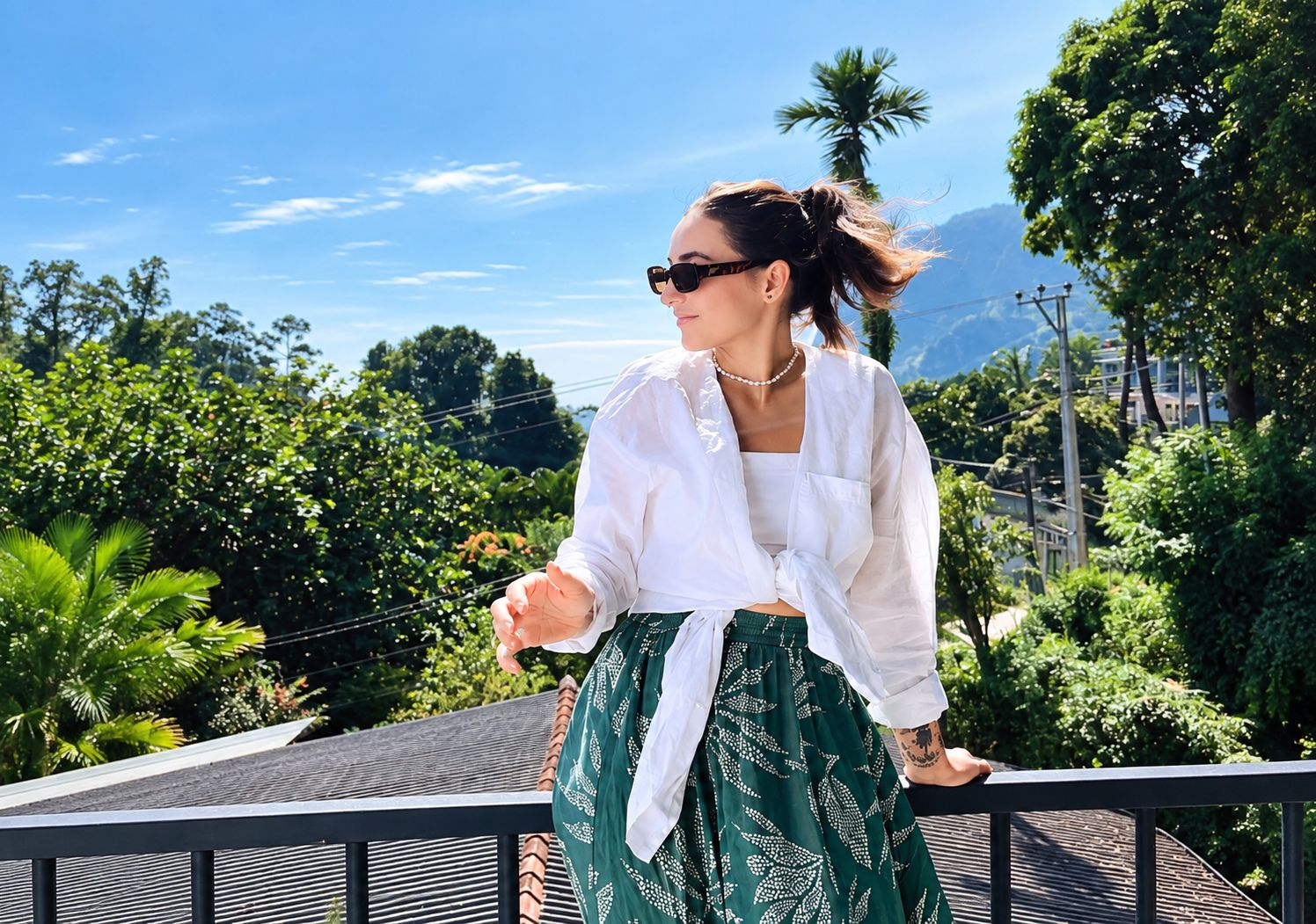 A person standing on a balcony with a view of greenery and mountains.