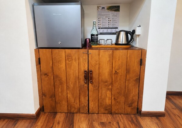 A wooden cabinet with a stainless steel appliance on top, a bottle, and a kettle on the counter. - Poomaz Peace Palace - Ella (Ella)
