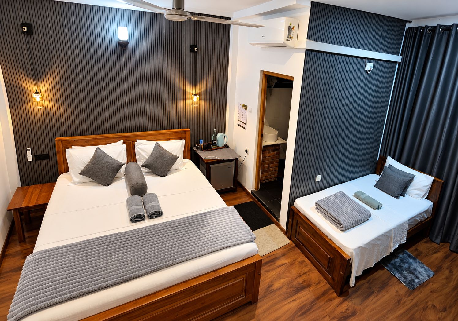 Habitación de hotel con una cama grande, una cama más pequeña, un escritorio, un armario y un ventilador de techo.