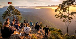 A group of people sitting on a rocky outcrop overlooking a mountainous landscape during sunset. - Poomaz Peace Palace - Ella (Ella)