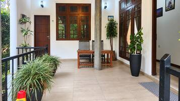 Um corredor espaçoso com um banco de madeira, plantas em vasos e uma grande janela com vista para o verde.