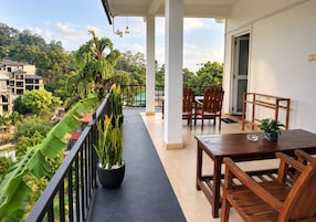 A balcony with a table and chairs, surrounded by potted plants and a view of the neighborhood.