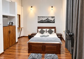 Un dormitorio con una cama de madera, dos mesitas de noche, una obra de arte en la pared y una cortina gris.