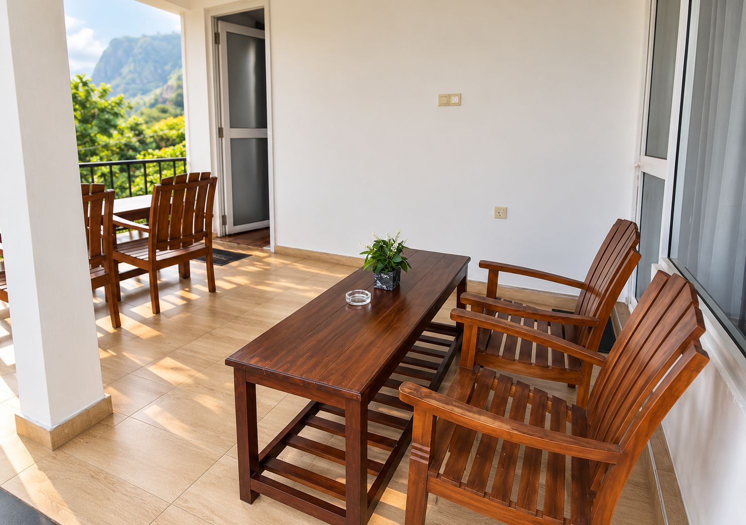 Un comedor con mesa y sillas de madera, una planta en maceta y vistas a montañas a través de una puerta.