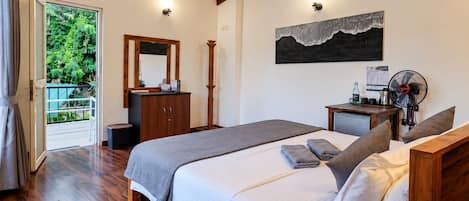 Een slaapkamer met een bed, een dressoir, een bureau, een ventilator en uitzicht op groen.