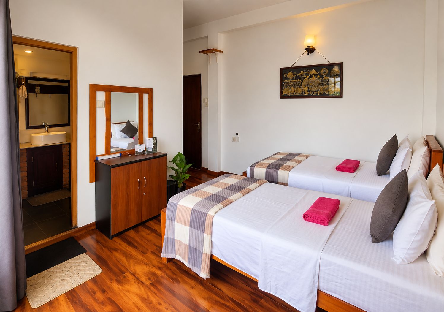Une chambre d’hôtel avec deux lits, une armoire en bois, une salle de bain avec un lavabo et un miroir, et un luminaire fixé au mur.