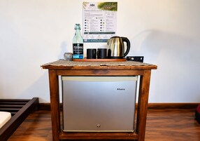A compact kitchenette with a wooden table, a coffee maker, a bottle of water, and a small refrigerator.