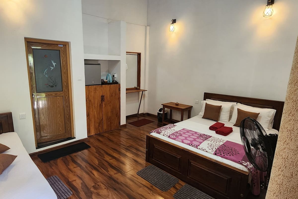 Une chambre avec un lit en bois, une armoire en bois, une petite table, une table de chevet, un ventilateur et une porte avec un panneau de verre.