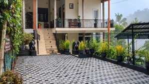 Un edificio de dos pisos con piso de diseño a cuadros, un balcón con plantas en macetas y una escalera que conduce al nivel superior.
