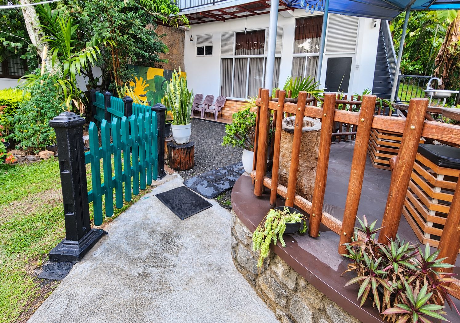 A garden pathway leading to a patio area with a wooden fence, potted plants, and outdoor furniture.