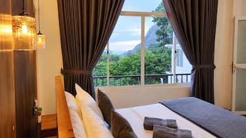 Habitación de hotel con cama, almohadas, vistas a zonas verdes y montañas, y una ventana con cortinas.