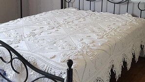 Ein Bett mit weißem Spitzenüberwurf, Metallgestell und Holzboden.