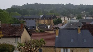 Ein Wohngebiet mit Steinhäusern, einem Baum mit weißen Blüten und einer Hügelkulisse im Hintergrund.