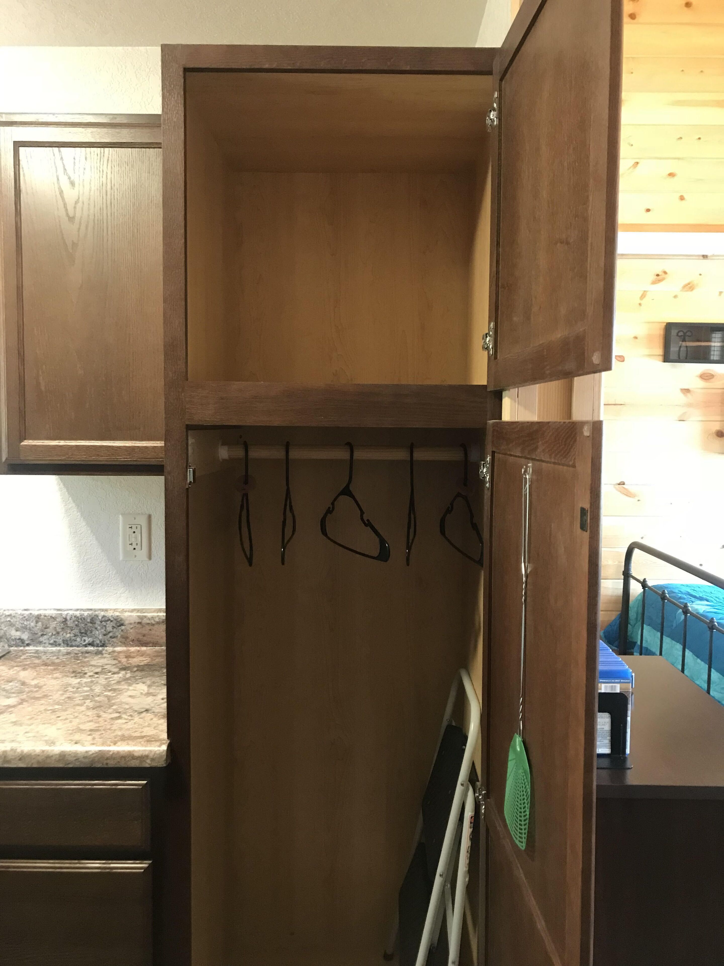 Un armario de madera con una barra para colgar y un objeto verde colgado en la puerta.