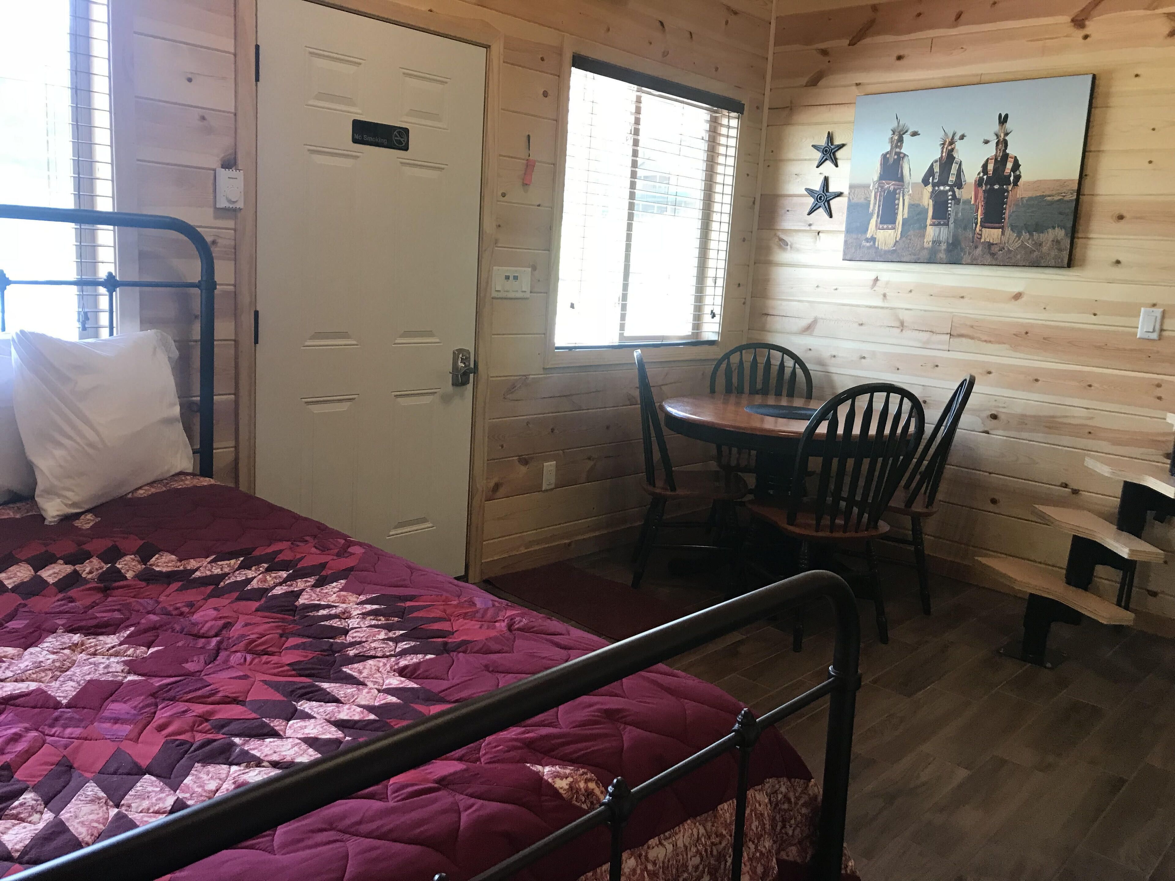 Ein Zimmer mit einem Bett, einem Esstisch mit Stühlen, einem Bild an der Wand und einer Tür mit einem Rauchverbot-Schild.