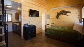 A wooden cabin interior with a bed, dresser, and TV.