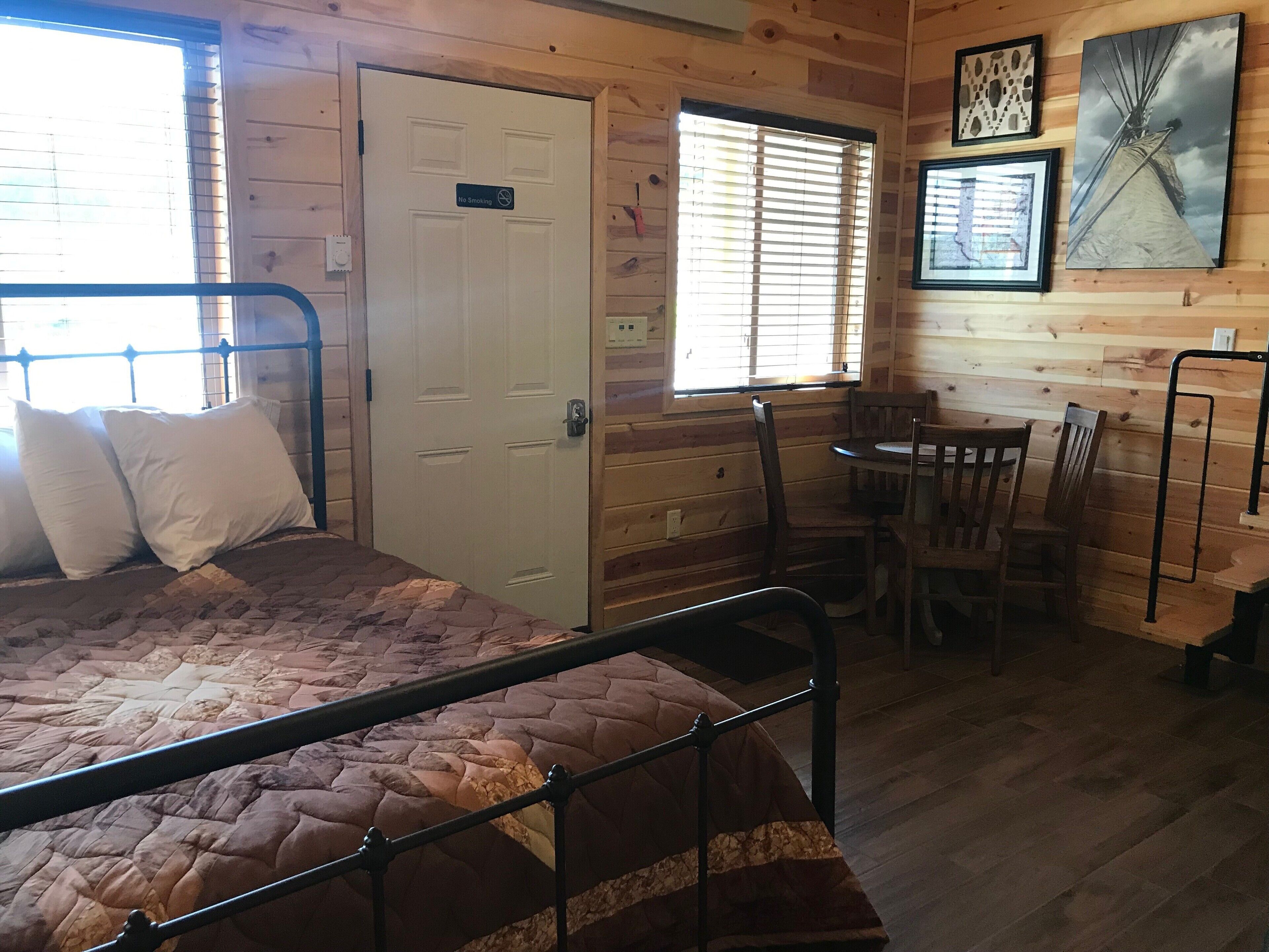 A wooden cabin room with a bed, a dining table, and chairs.