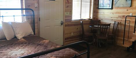 A wooden cabin room with a bed, a dining table, and chairs.