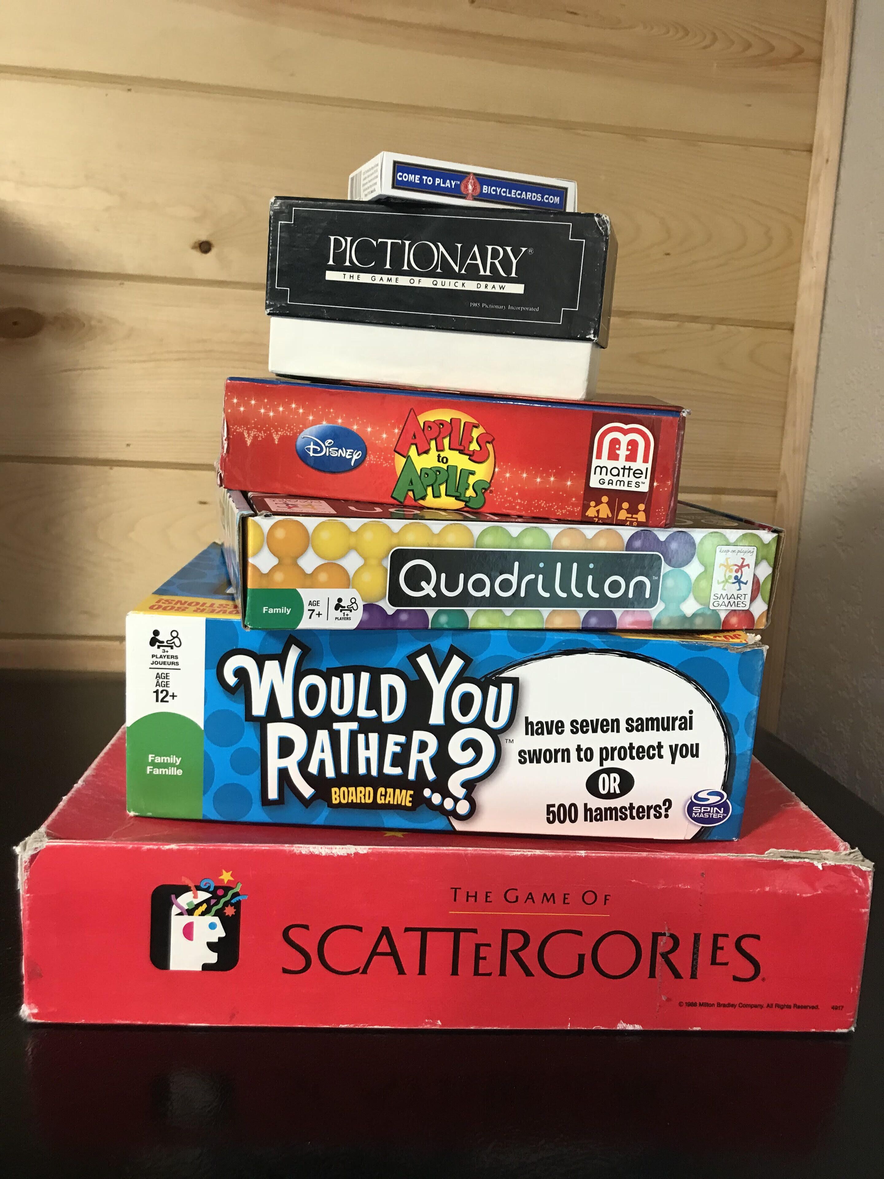 A stack of board games including Pictionary, Apples to Apples, and Scattergories.