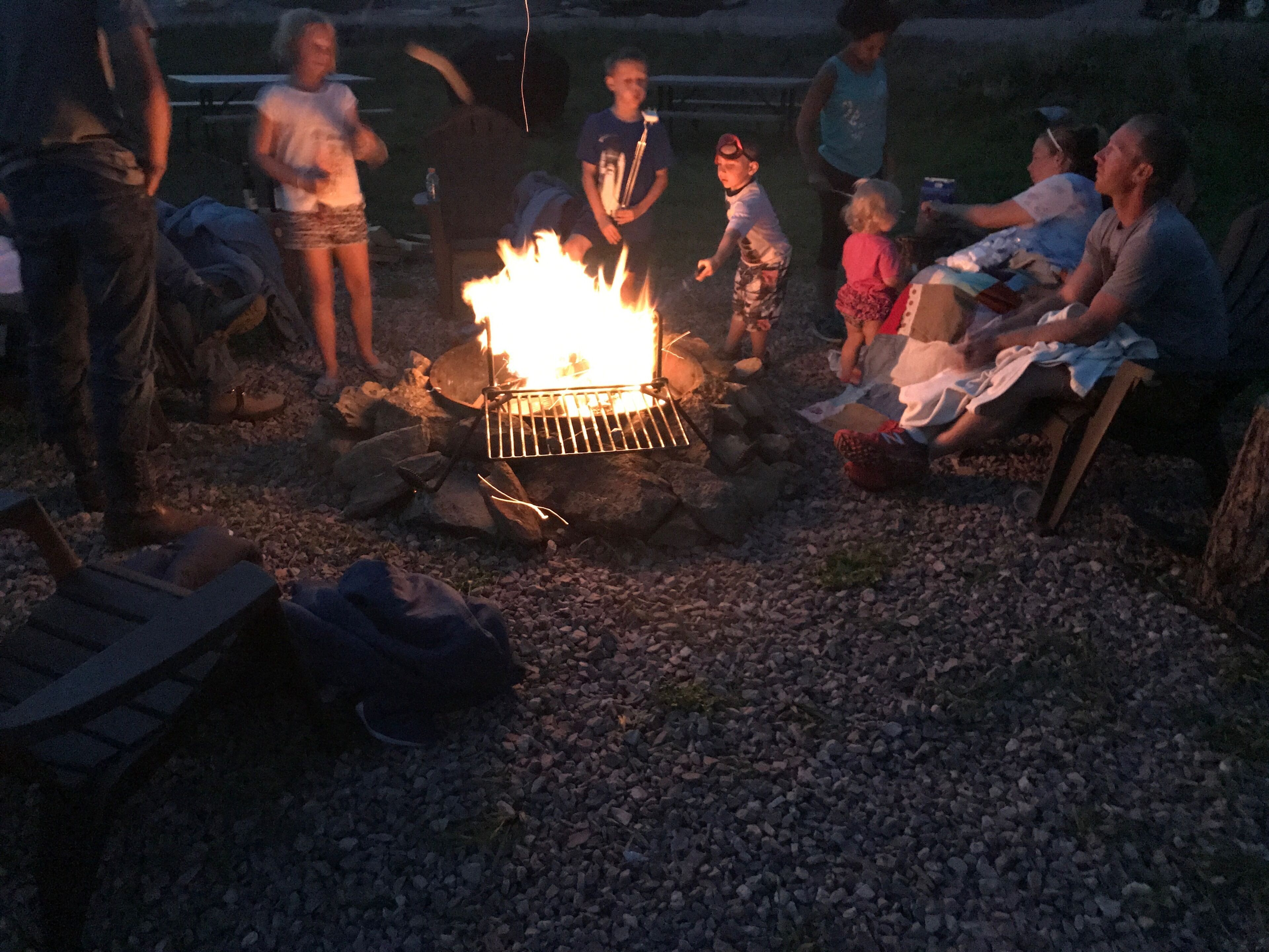 Un groupe de personnes s’est rassemblé autour d’un feu de camp dans un cadre en plein air.