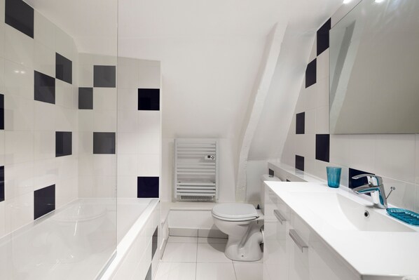 Ein modernes Badezimmer mit Wand in Schwarz und Weiß gefliest, einer weißen Badewanne, einer weißen Toilette und einem weißen Waschbecken mit blauer Glasablage.