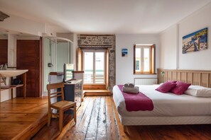Ein Schlafzimmer mit Bett, Sessel, Schreibtisch, Waschbecken und Fenster.