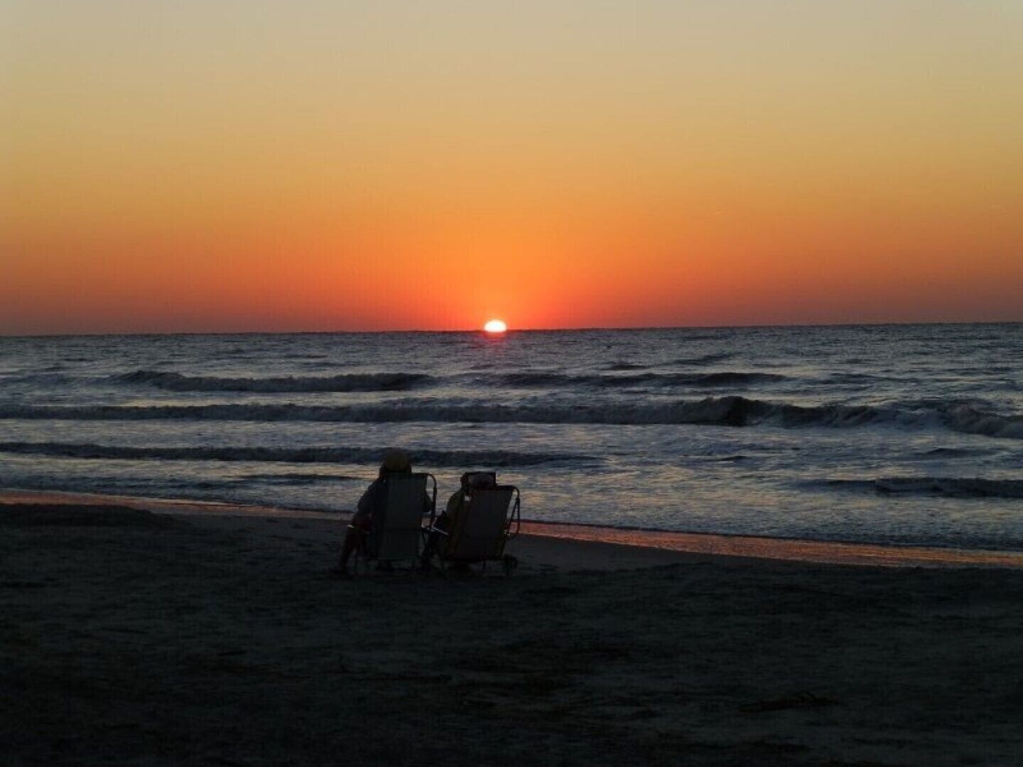 Dos personas sentadas en sillas de playa mirando el océano al atardecer.