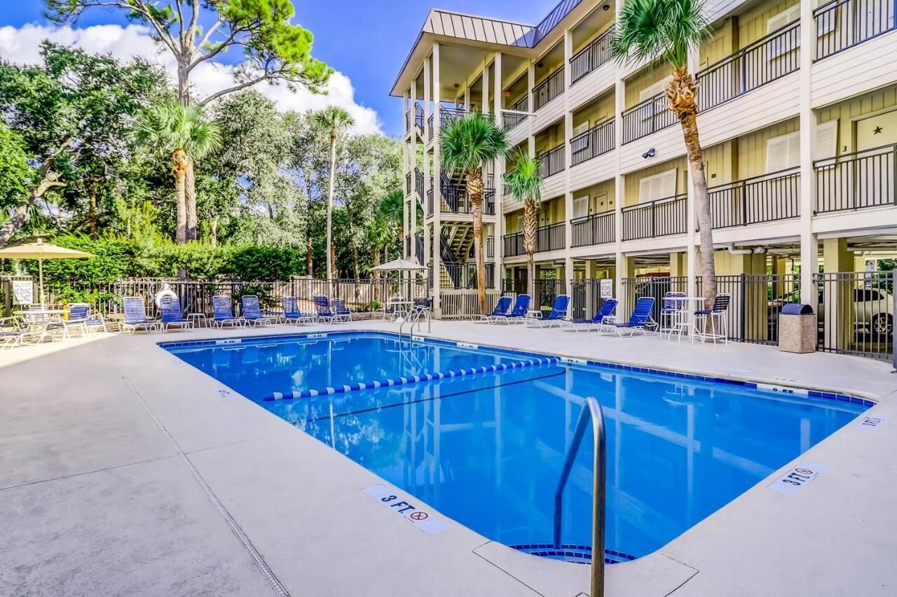 A swimming pool with lounge chairs and a multi-story building with balconies.