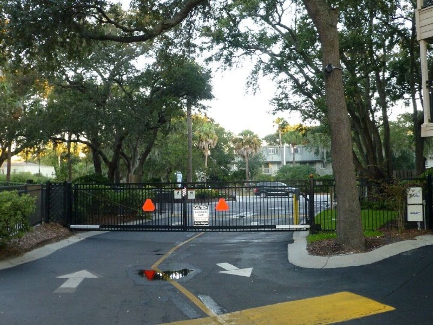 Una strada privata con cancello, cordolo giallo e frecce direzionali sull'asfalto.