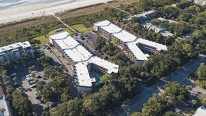 An aerial view of a coastal hotel complex with multiple buildings, parking areas, and a beach in the background. - Beautiful Ocean View - Walk to Coligny (Hilton Head Island)
