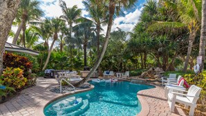 A pool area with a curved design, surrounded by palm trees and a brick patio.