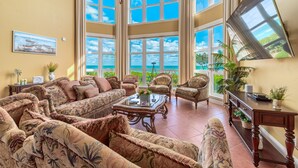 A spacious living room with large windows, a comfortable sofa set, a coffee table, and a television on a stand.