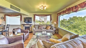 A cozy living room with a fireplace, comfortable seating, and a large window offering a view of trees. - Waterfront Home ~ 6 Mi to Olympic National Park! (Port Angeles)