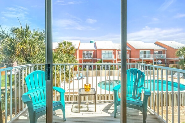 A balcony with turquoise chairs, a small table with a yellow object, and a pool in the background.