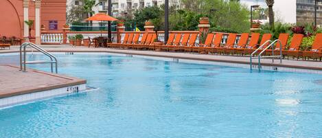 A swimming pool with orange lounge chairs and a palm tree in the background.