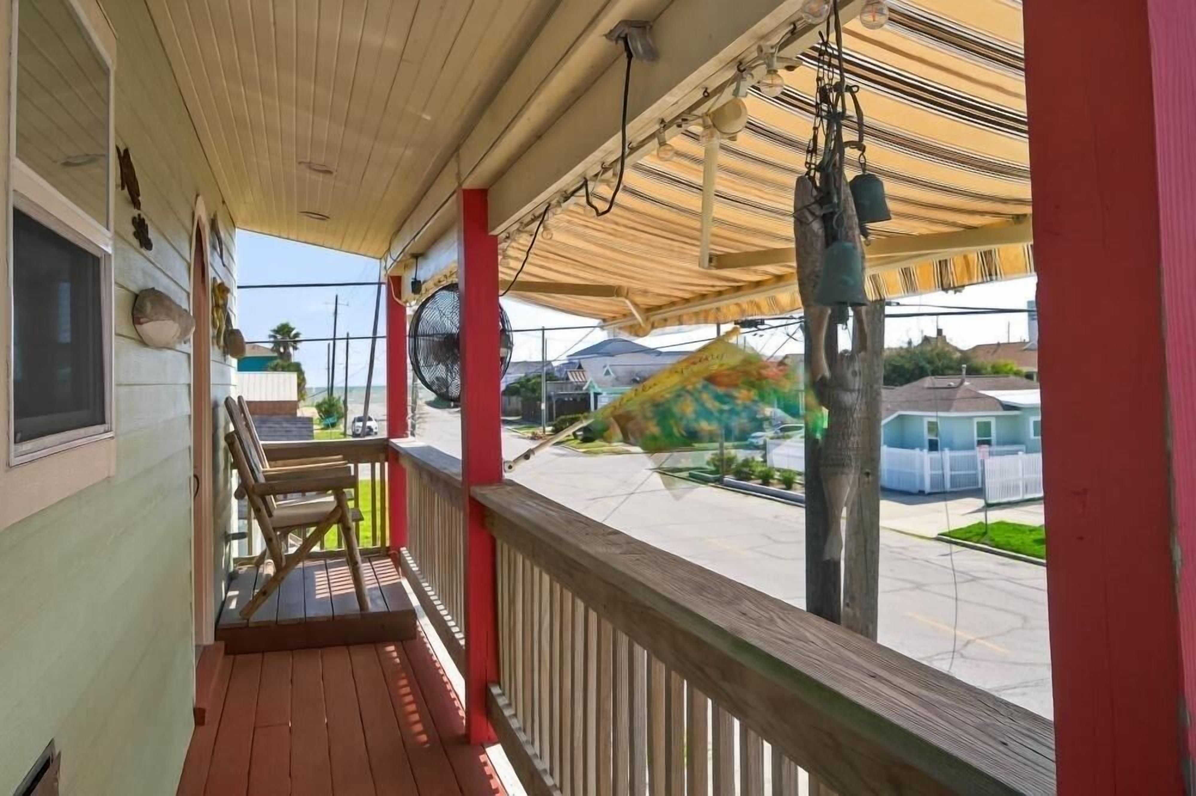 A covered porch with a wooden railing, a fan, and a hammock.