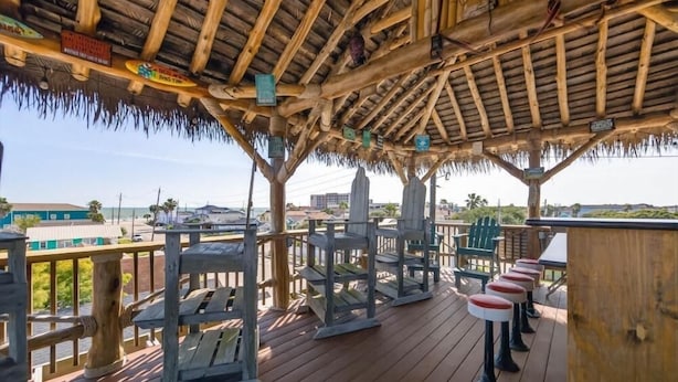 Eine Holzterrasse mit einem Reetdach, Sitzgelegenheiten im Freien und Blick auf das Meer.