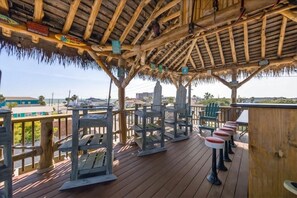 A wooden deck with thatched roof, outdoor seating, and a view of the ocean. - Pet-friendly home located near Seawall. (Galveston)