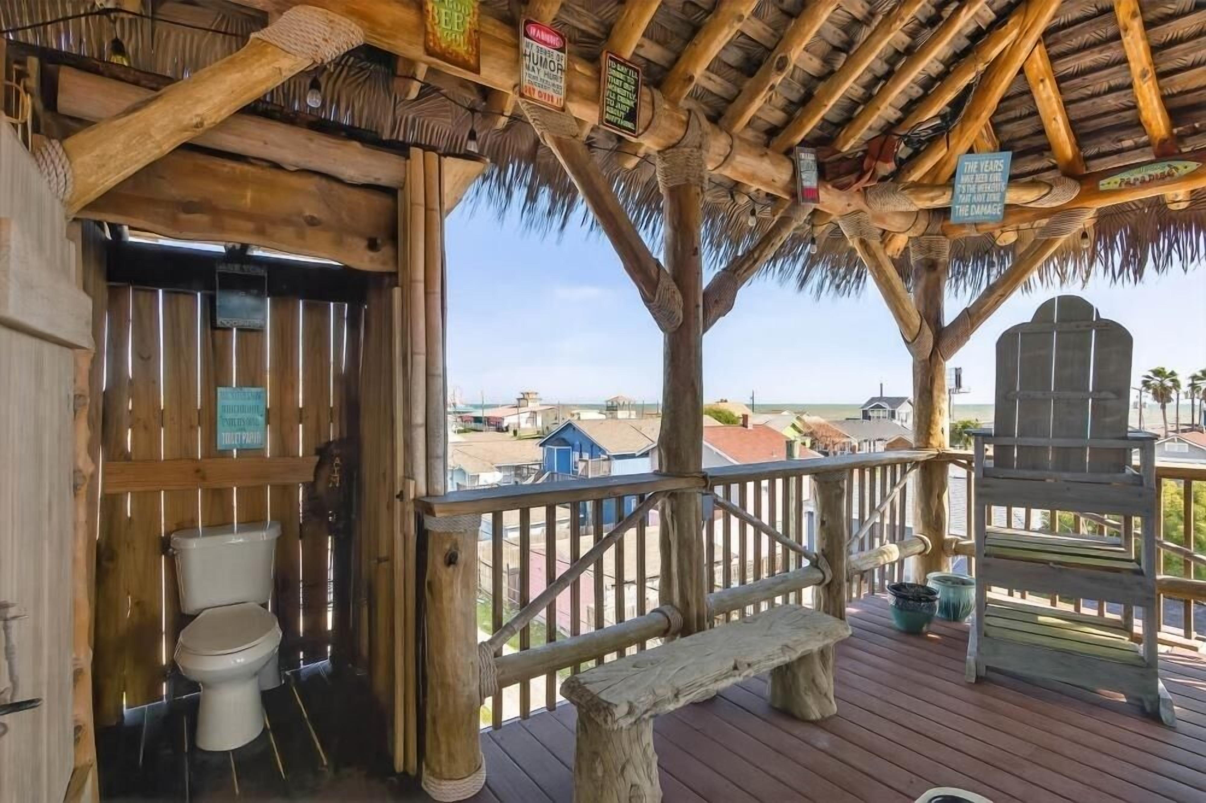 A wooden deck with a thatched roof, a toilet, and a bench.