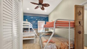 Ein Schlafraum mit Etagenbetten, Deckenventilator, Holzschrank und Fenster mit Jalousien.
