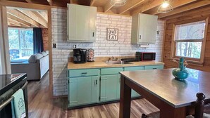 A cozy cabin-style kitchen with wooden beams, a brick backsplash, and a dining area with a table and chairs. - Hidden Gem in the woods with hot tub  (Berkeley Springs)
