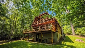 A rustic cabin with a wooden exterior, a balcony, and a large window. - Hidden Gem in the woods with hot tub  (Berkeley Springs)