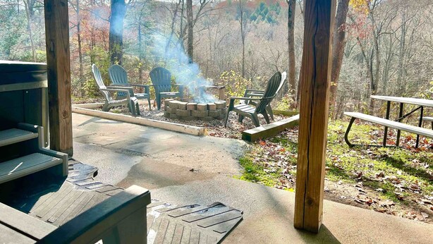 An outdoor seating area with Adirondack chairs and a fire pit, surrounded by trees and a wooden deck. - Hidden Gem in the woods with hot tub  (Berkeley Springs)